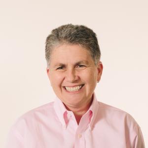 Dr. Vitka Eisen smiling at the camera in front of a peach background